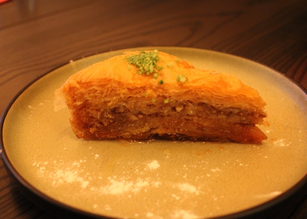  Slice of classic Greek Baklava dessert with pistachios, served on a round plate at Greek Theory