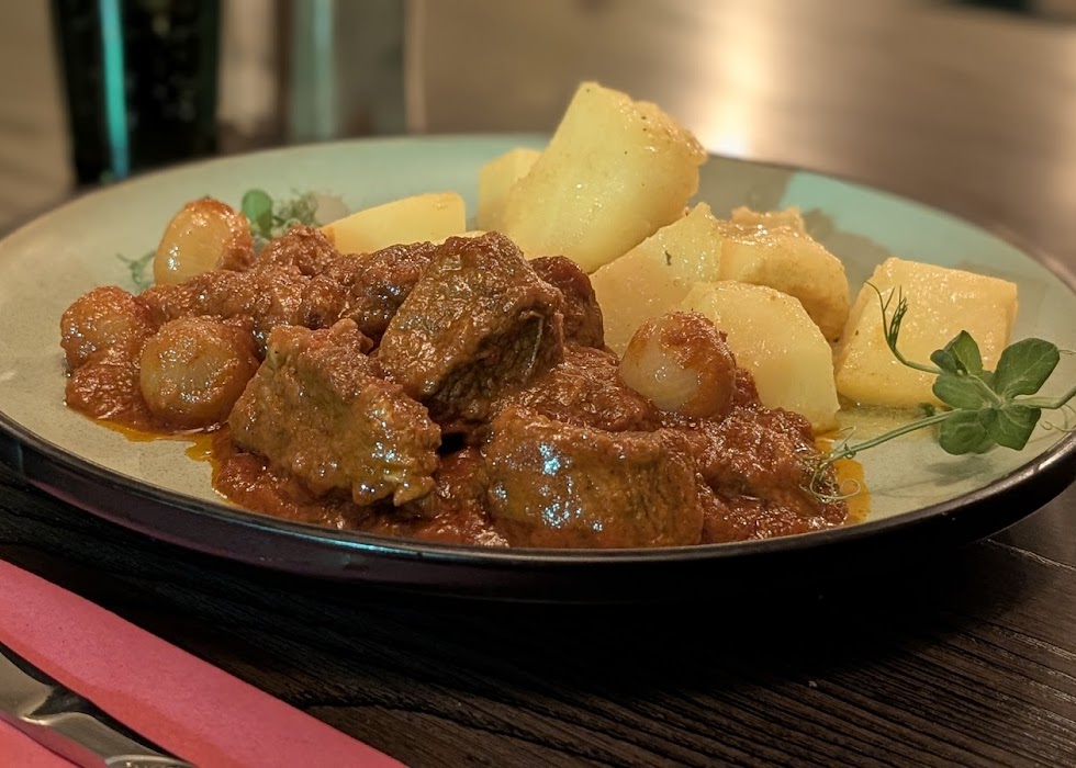 Hearty Greek Beef Stifado stew with whole pearl onions and rich tomato 
sauce, served with potatoes at Greek Theory, Falkirk 