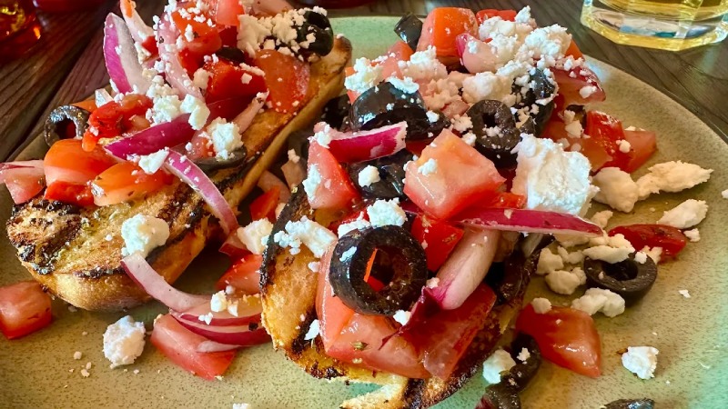  Greek bruschetta topped with fresh tomatoes, crumbled feta, sliced olives, and 
red onion, served at Greek Theory Falkirk