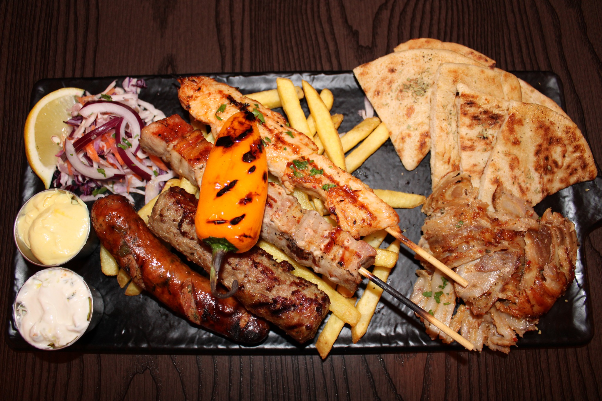 Greek Mixed Grill Platter from Greek Theory Falkirk, featuring gyros, souvlaki 
skewers, sausage, kebab, salad, pita, and two dipping sauces 